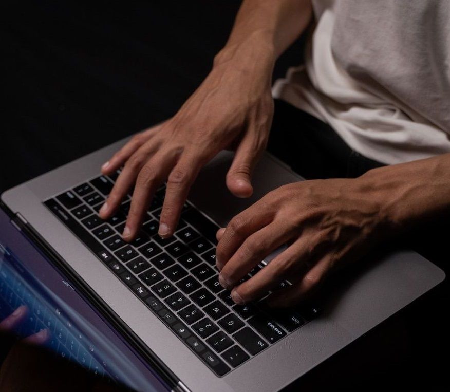 A photo of a man's hands on the keyboard of a laptop.